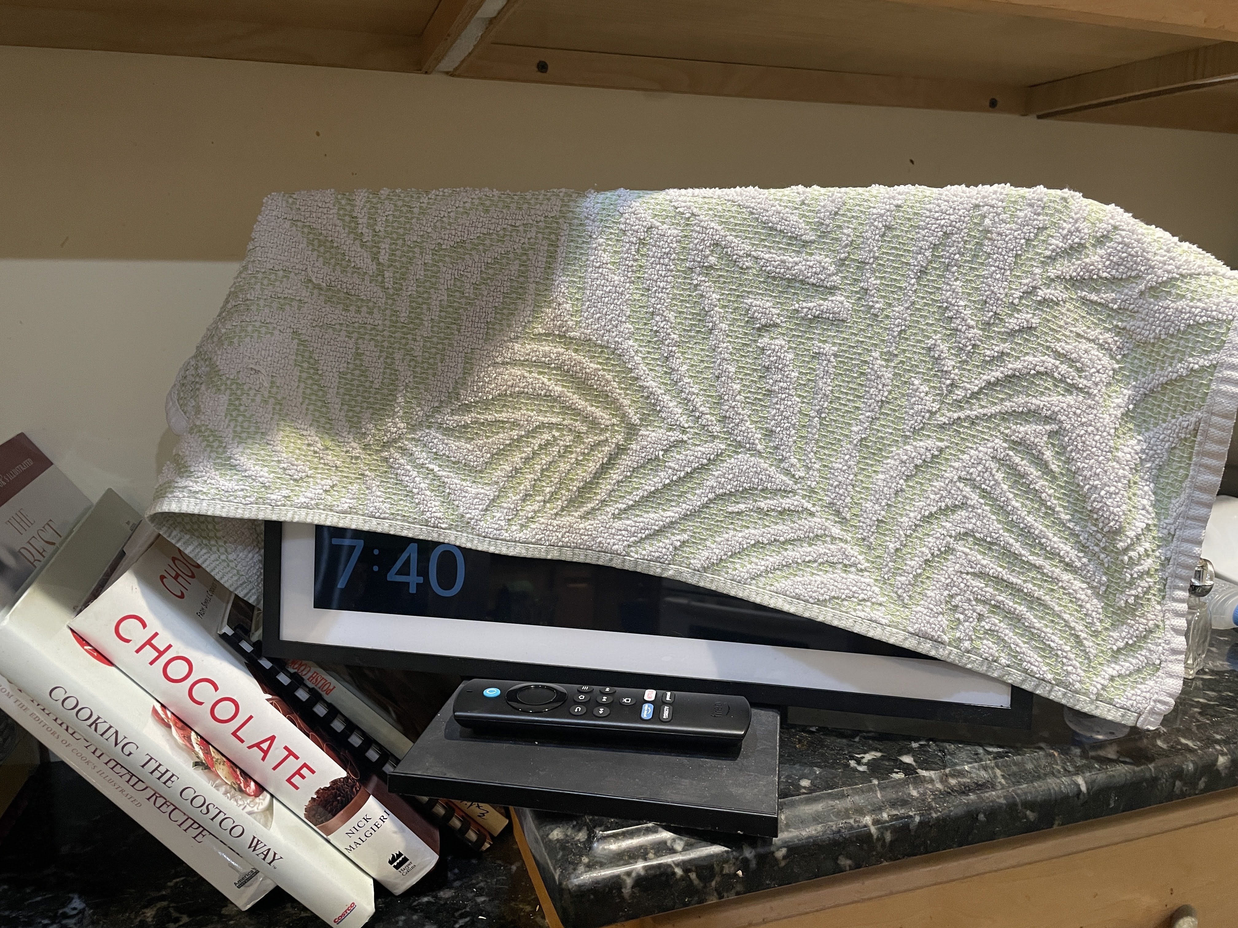 An ‘Amazon Echo Show 15’ digital display with a hand towel thrown over most of the screen. The ‘Sleep mode’ leaves a clock in the bottom left corner, which was left exposed with how the towel is draped over the device.